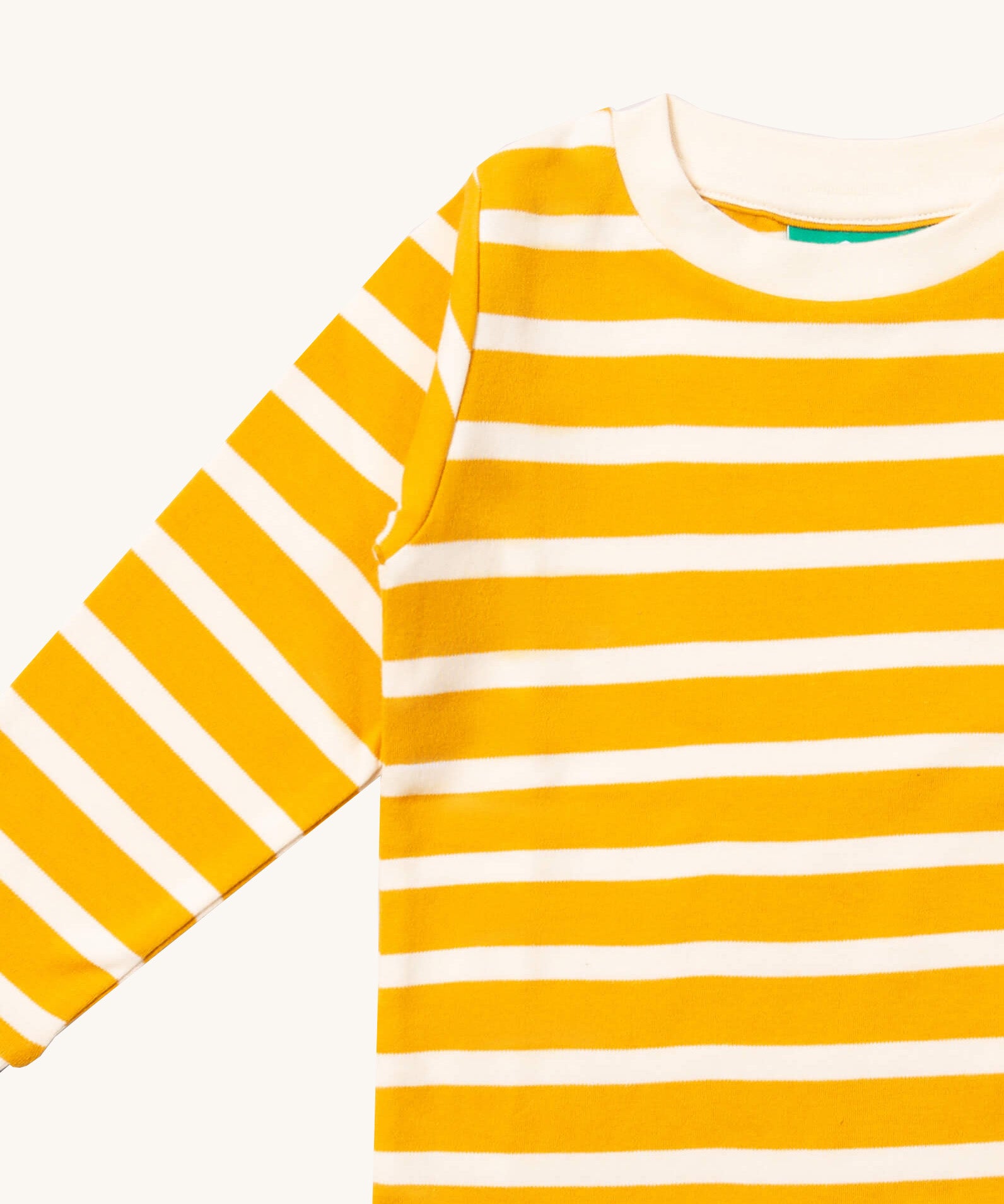 A close up of the Little Green Radicals gold striped long sleeve top that's available at Babipur. Showing the yellow and white stripe detail on organic cotton fabric.