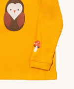 A close up of the Little Green Radicals gold brown owl applique long sleeve top showing the mushroom applique detail on dark yellow organic cotton fabric.