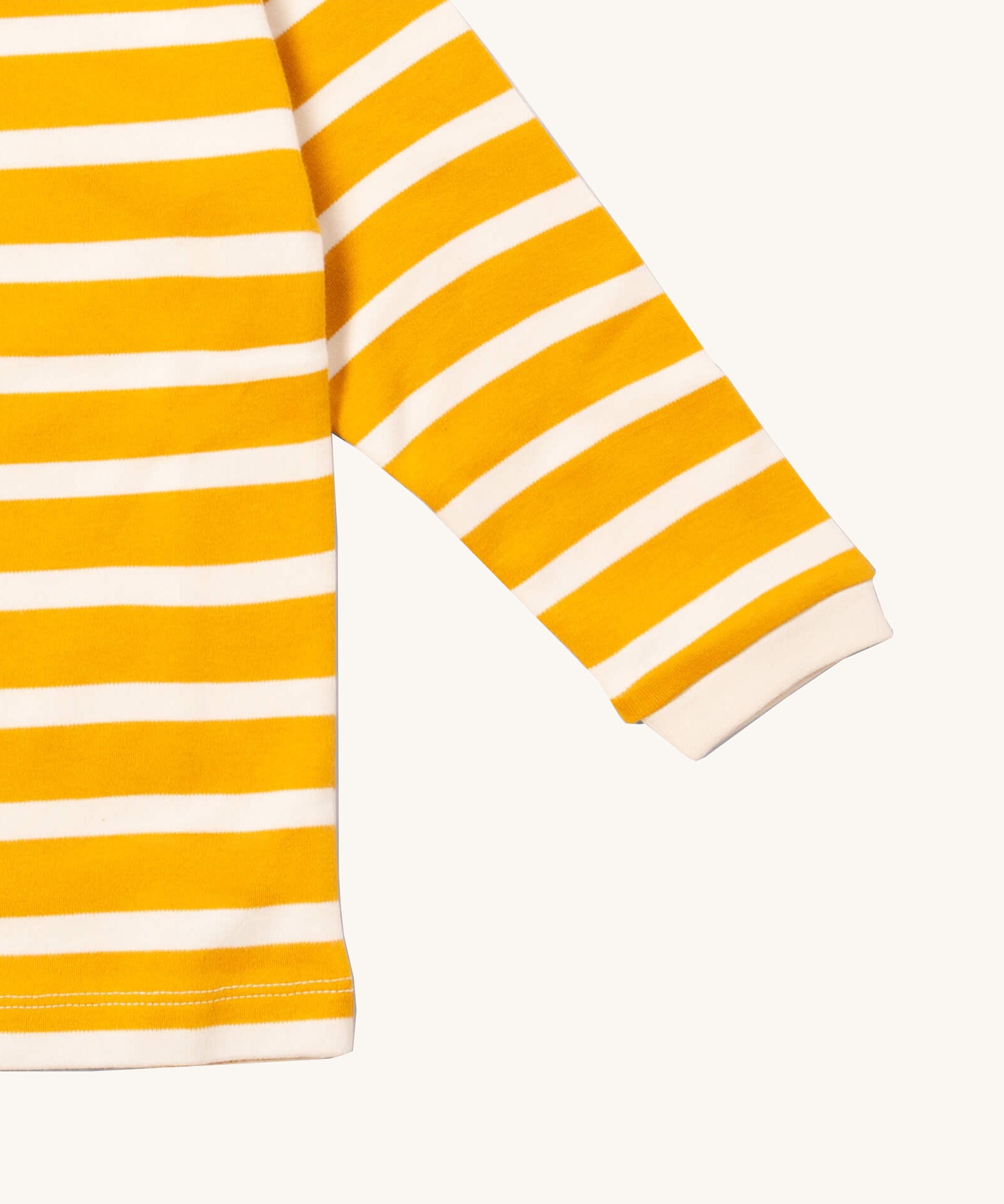 A close up of the Little Green Radicals gold striped long sleeve top that's available at Babipur. Showing the white cuff detail on striped organic cotton fabric.