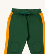 A close up the Little Green Radicals olive cosy joggers showing the drawstring detail, 2 side pockets and stitched on knee patches  on green organic cotton fabric.