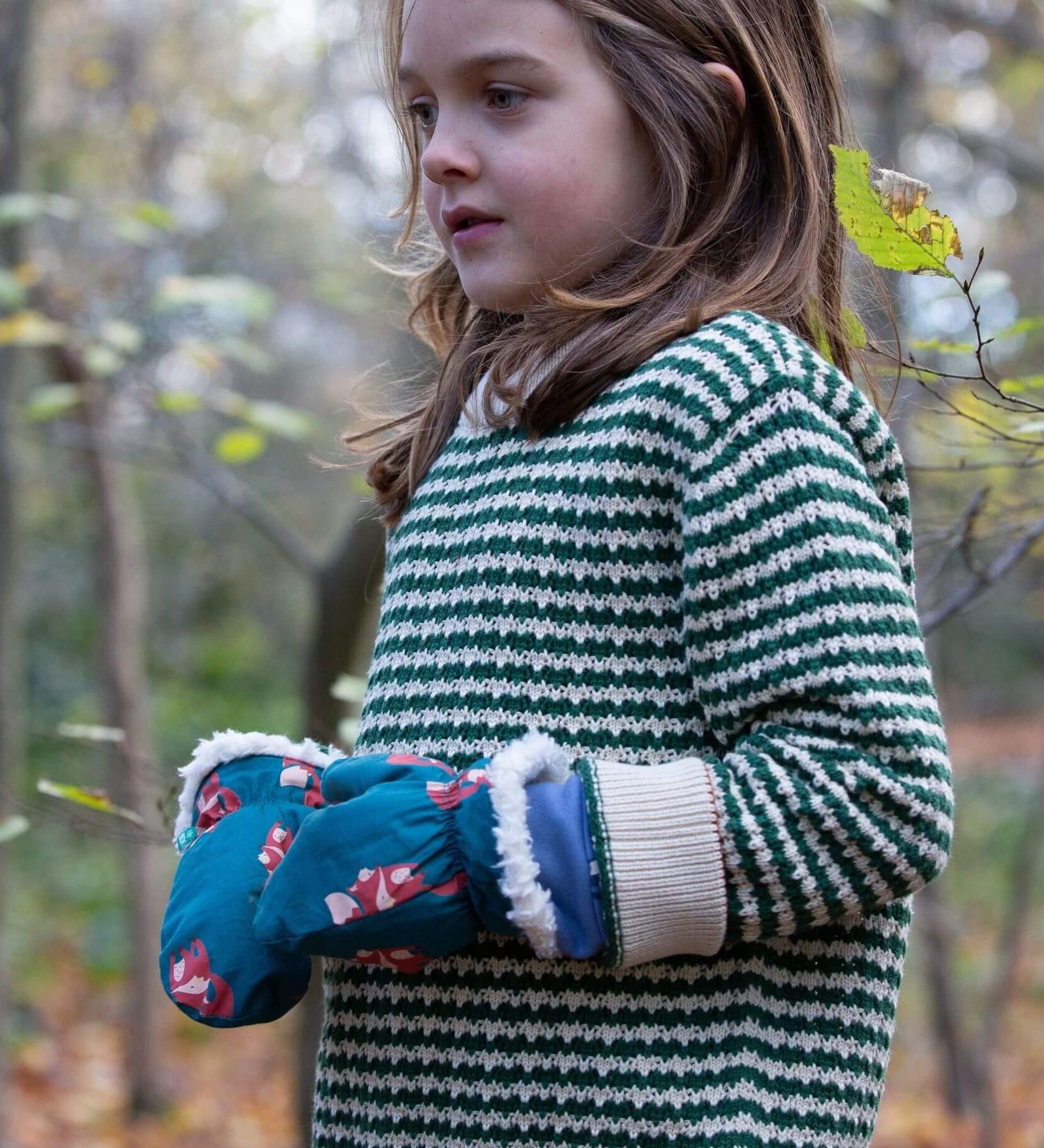 A child wearing the Little Green Radicals snuggly knitted jumper in olive stripe. Showing the knitted detail and cream cuff on green and cream striped GOTS organic cotton fabric available a at Babipur.