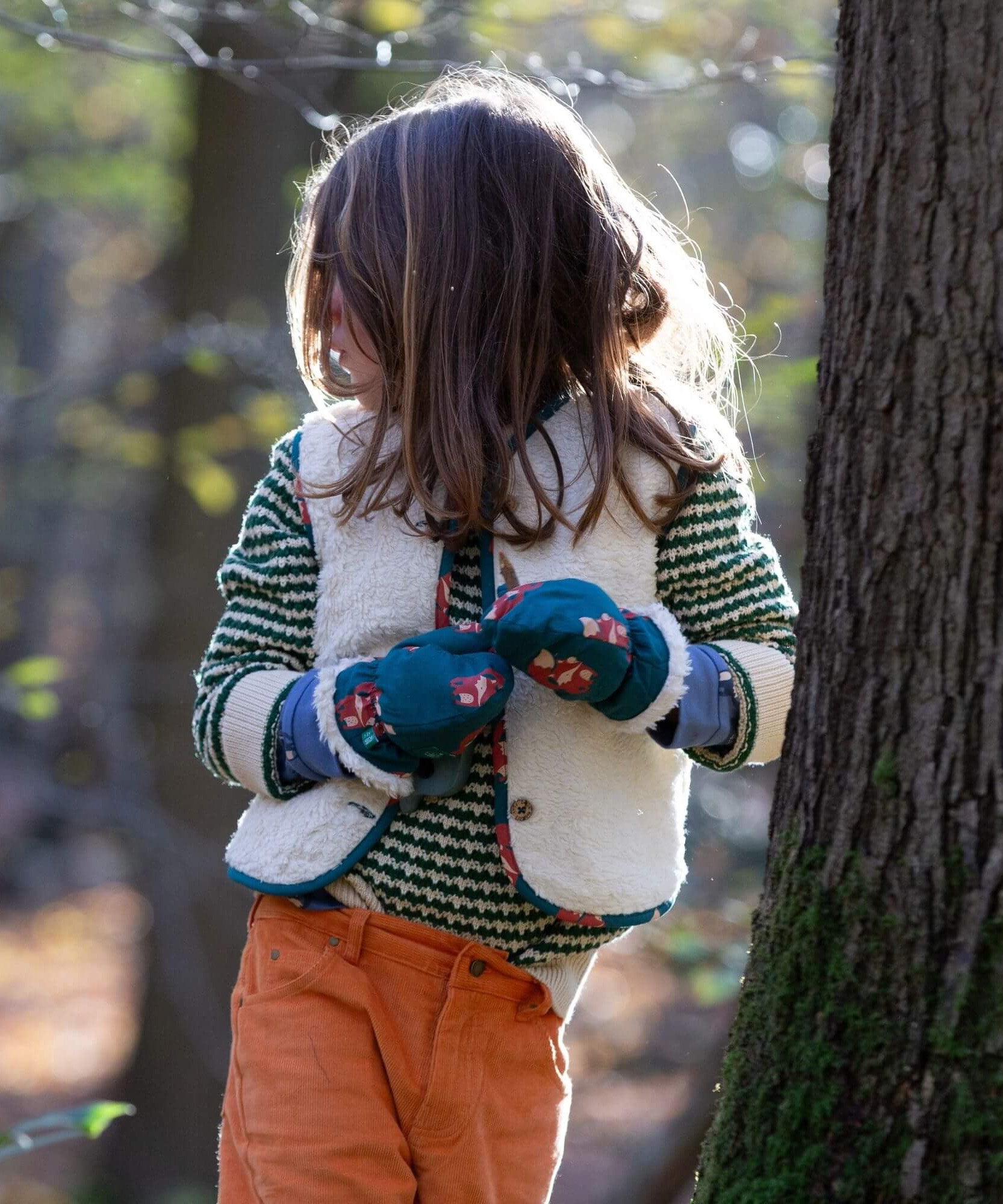 A child wearing the Little Green Radicals snuggly knitted jumper in olive stripe with a reversible sherpa fleece fox gilet on top making a warm outfit
