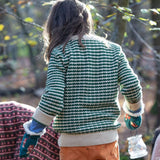 A child wearing the Little Green Radicals snuggly knitted jumper in olive stripe available at Babipur. Features a cream collar, turned up cuff and hem on green and cream striped GOTS organic cotton fabric.