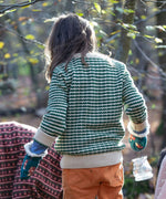 A child wearing the Little Green Radicals snuggly knitted jumper in olive stripe available at Babipur. Features a cream collar, turned up cuff and hem on green and cream striped GOTS organic cotton fabric.