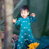 A child playing in the woods and wearing the Little Green radicals turquoise rainbow baby grow. A soft GOTS organic cotton all in one in turquoise with long sleeves 