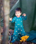 A child playing in the woods and wearing the Little Green radicals turquoise rainbow baby grow. A soft GOTS organic cotton all in one in turquoise with long sleeves 
