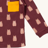 A close up of the Little Green Radicals brown bear sleeve t-shirt. Showing the elasticated cuff detail and yellow pouch pocket detail on dark maroon organic cotton fabric