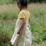 Girl walking in a grass field wearing the little green radicals short sleeve sunshine and rainbows easy peasy dress