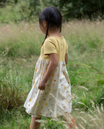 Girl walking in a grass field wearing the little green radicals short sleeve sunshine and rainbows easy peasy dress
