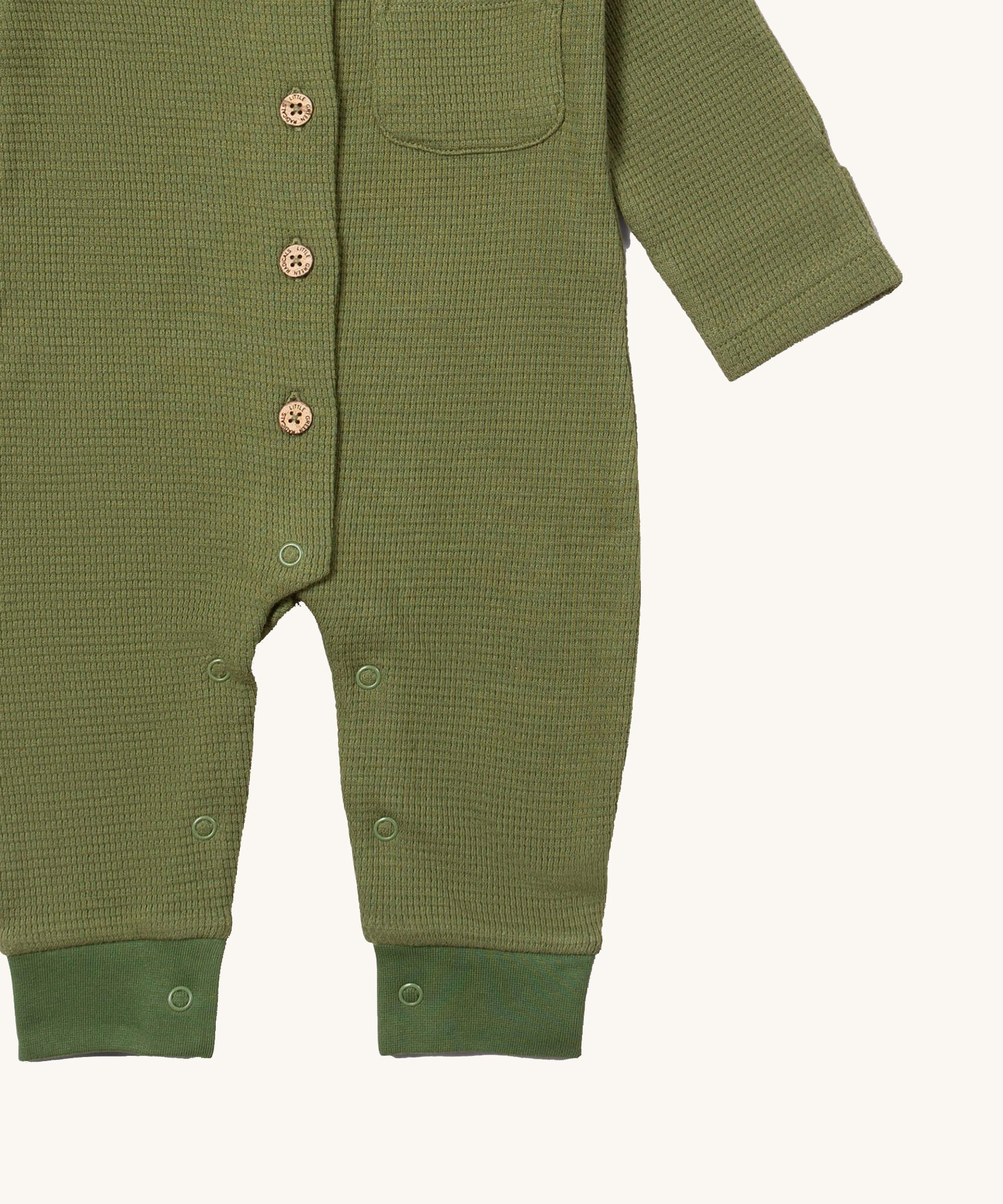 A close up of the Little Green Radicals green chive waffle playsuit showing the button and popper fastener detail on green waffle organic cotton fabric