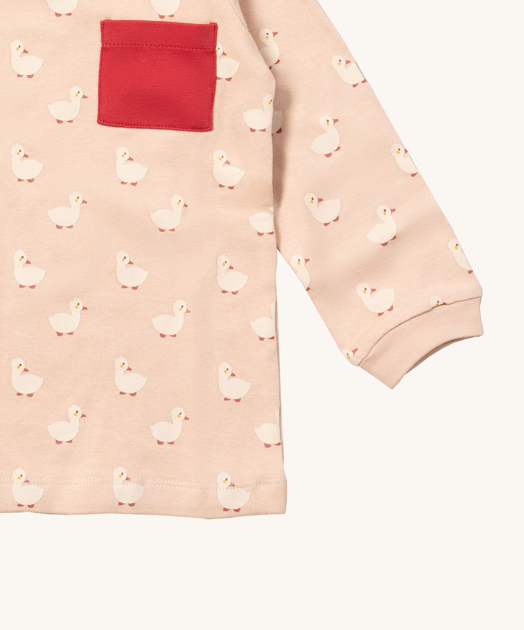 A close up of the Little Green Radicals puddle ducks sleeve t-shirt. Showing the cute duck prints and red pouch pocket detail on peach organic cotton fabric