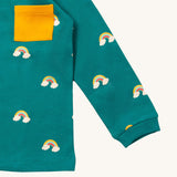 A close up of the Little Green Radicals turquoise rainbows long sleeve t-shirt. Showing the rainbow on clouds print and yellow chest pocket detail on turquoise organic cotton fabric.
