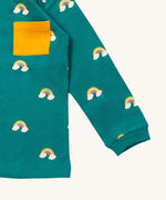 A close up of the Little Green Radicals turquoise rainbows long sleeve t-shirt. Showing the rainbow on clouds print and yellow chest pocket detail on turquoise organic cotton fabric.