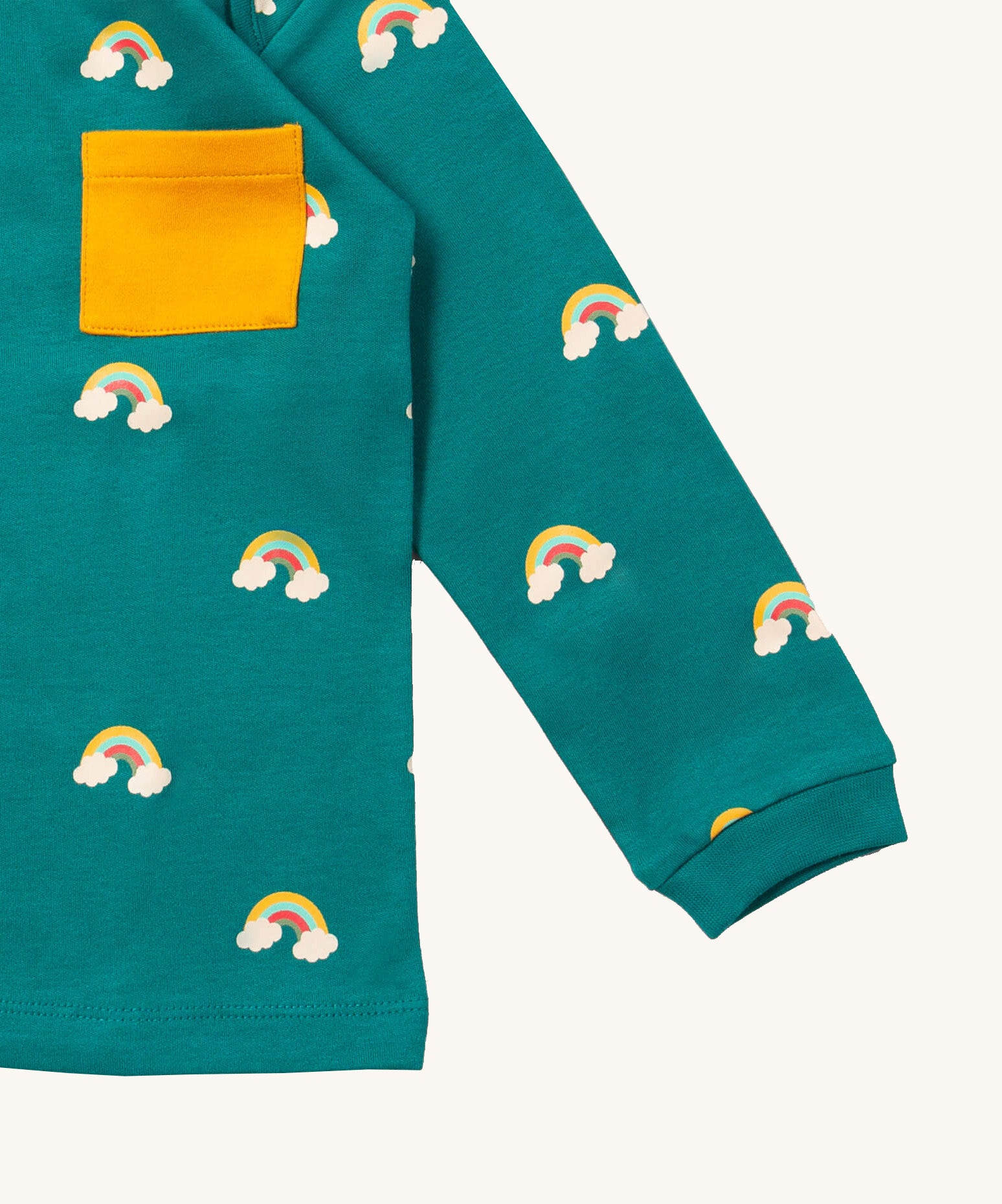 A close up of the Little Green Radicals turquoise rainbows long sleeve t-shirt. Showing the rainbow on clouds print and yellow chest pocket detail on turquoise organic cotton fabric.