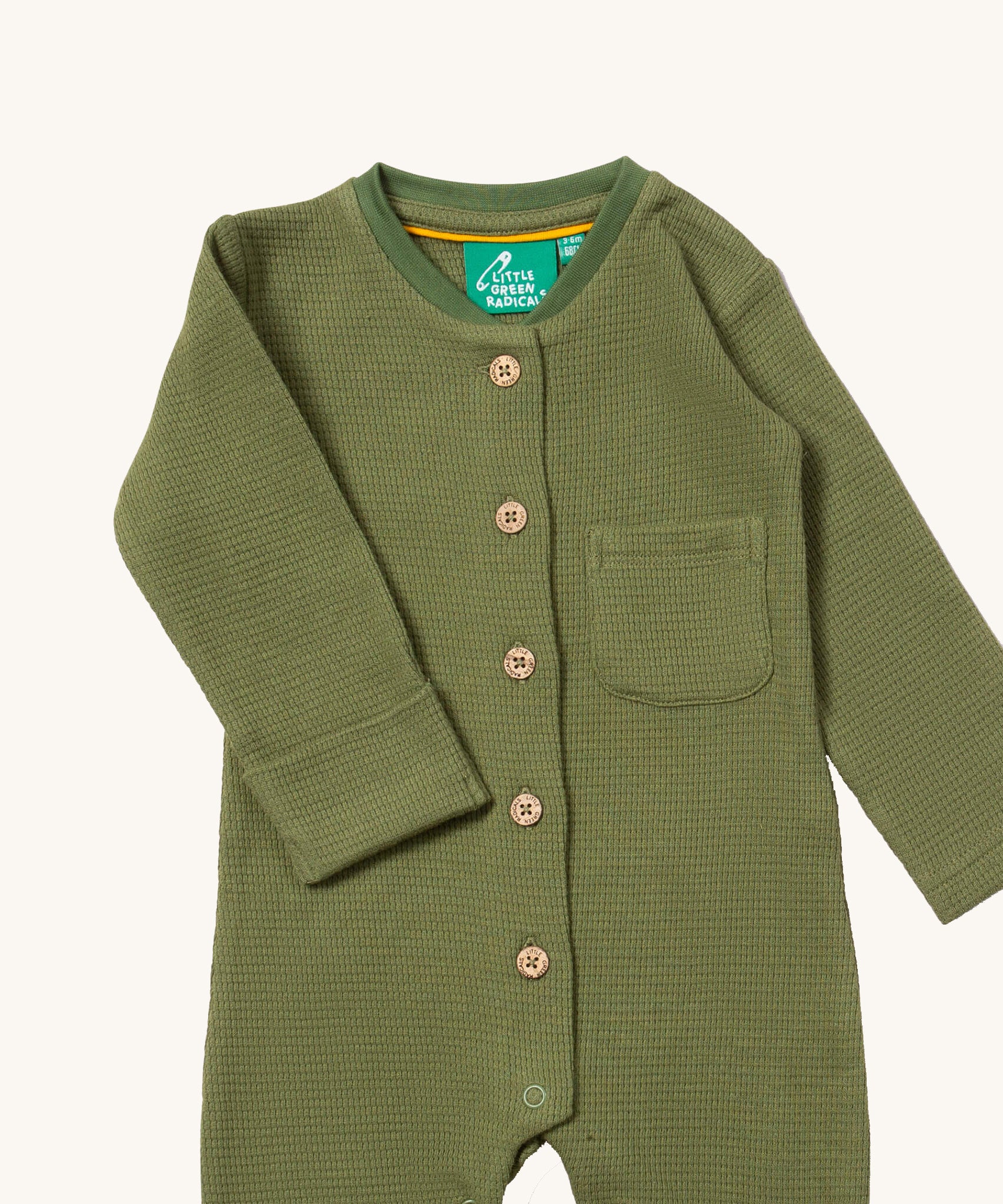 A close up of the Little Green Radicals green chive waffle playsuit showing the button fasteners and pocket detail on green organic cotton fabric