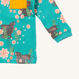A close up of the Little Green Radicals winter rabbits long sleeve t-shirt. Showing the rabbits in pink flowers print and yellow chest pocket detail on turquoise organic cotton fabric.