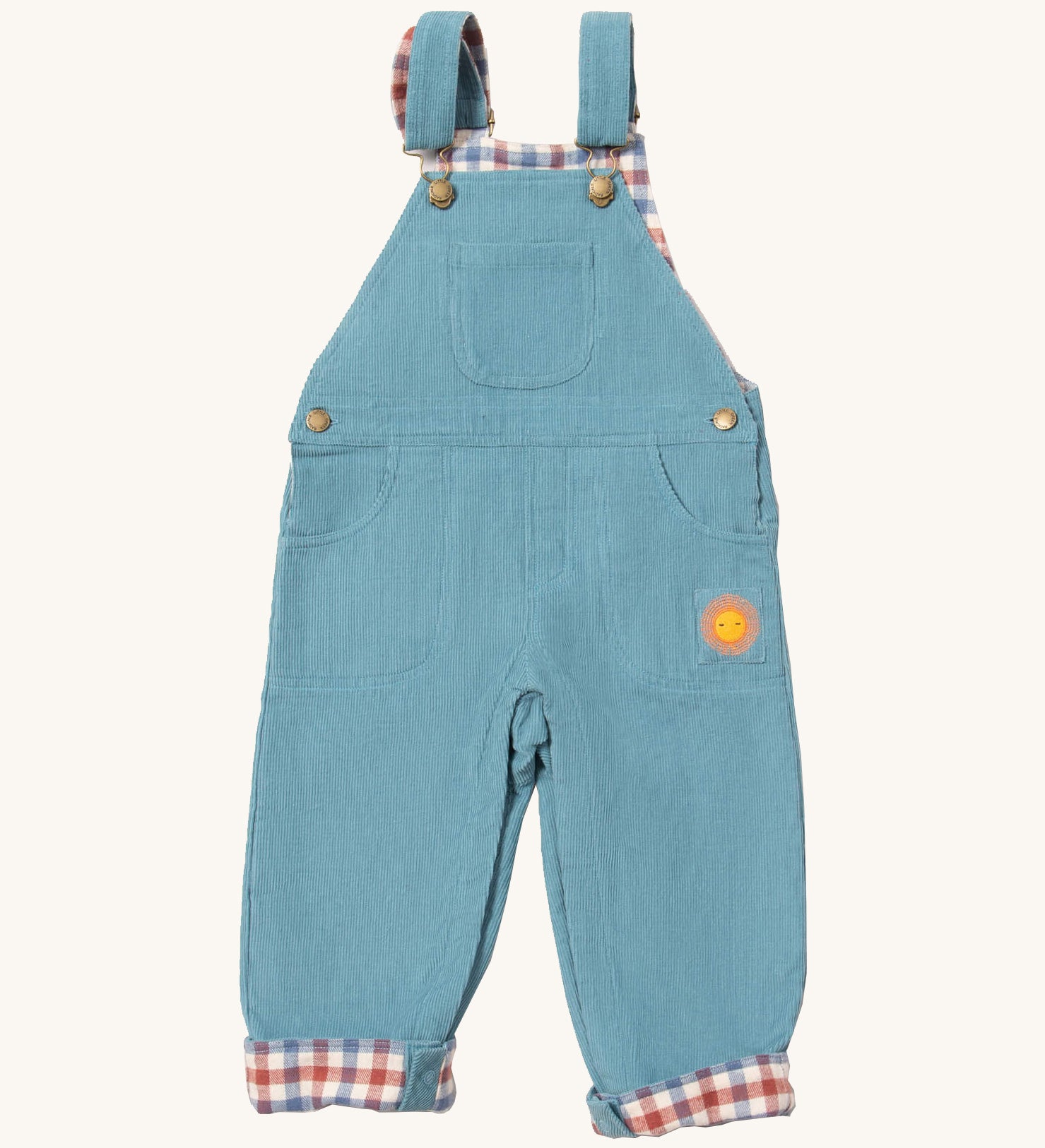 Little Green Radicals pale blue lined corduroy dungarees available at Babipur. A GOTS organic cotton dungaree in a corduroy style with a check inner. Features a small check pocket and 2 side pockets with a sun embroidery under the pocket 
