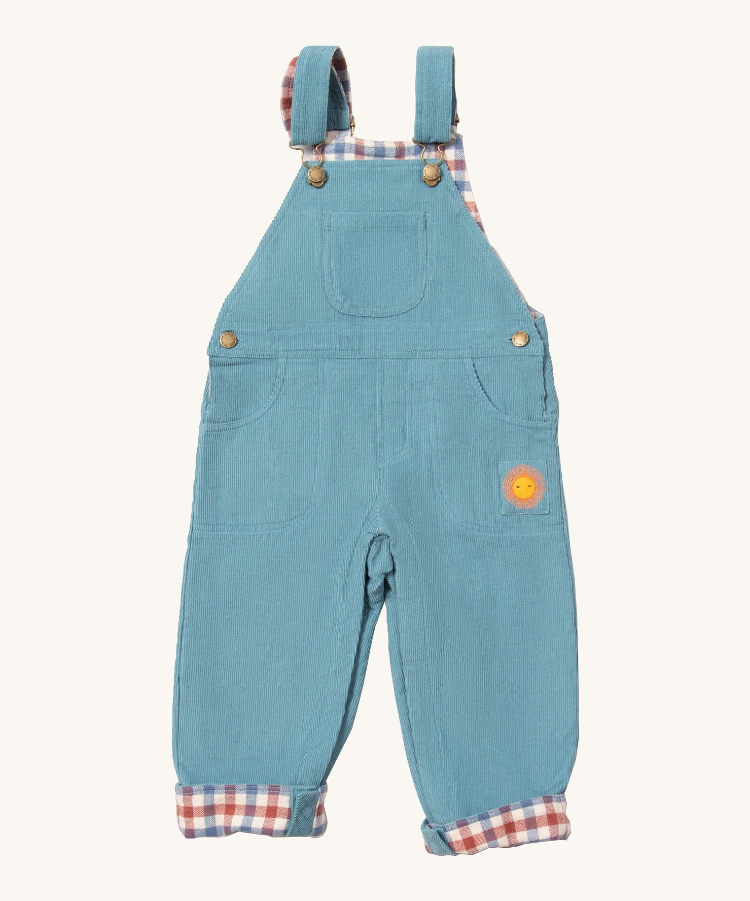 Little Green Radicals pale blue lined corduroy dungarees available at Babipur. A GOTS organic cotton dungaree in a corduroy style with a check inner. Features a small check pocket and 2 side pockets with a sun embroidery under the pocket 