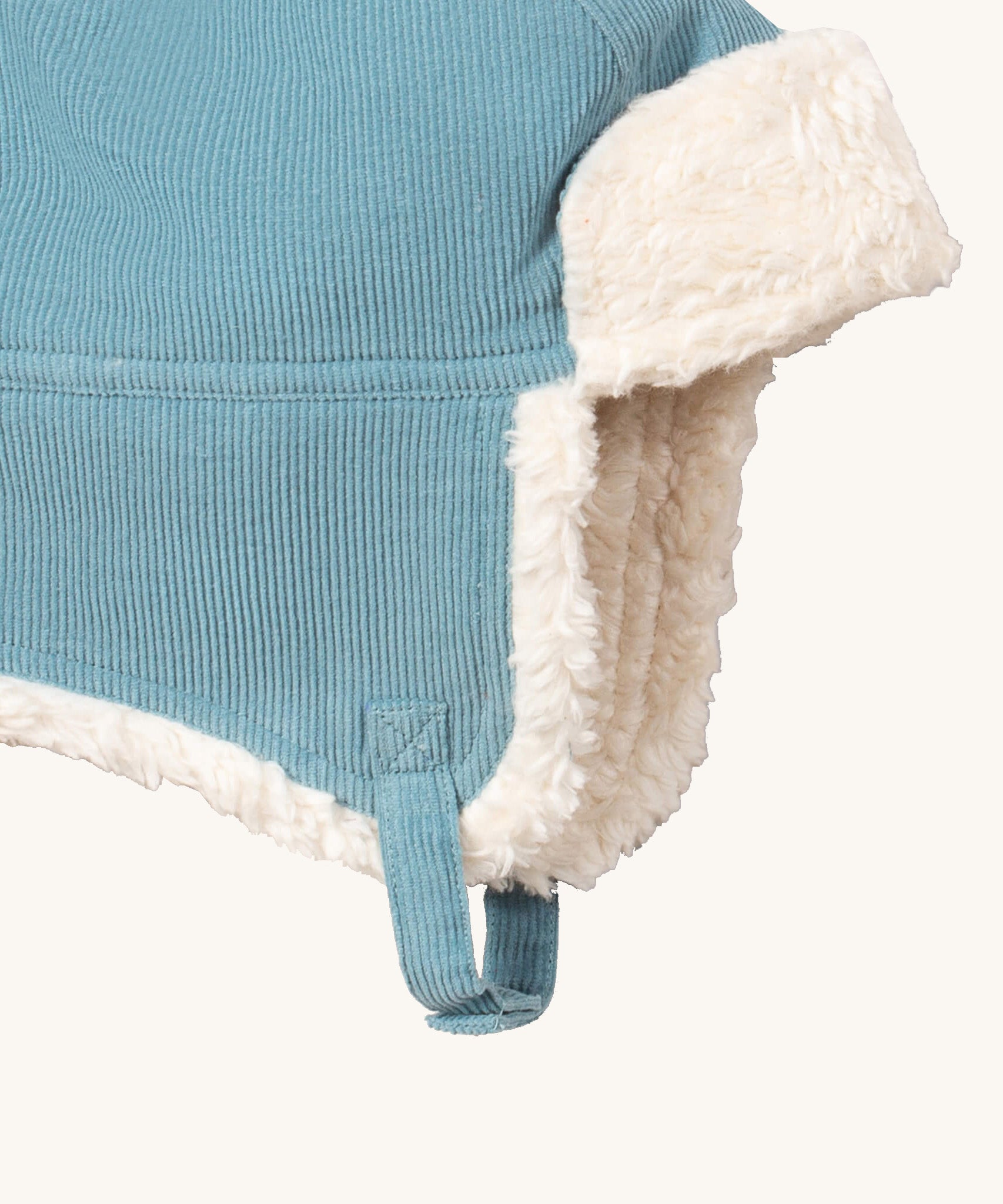 A close up of the Little Green Radials sherpa fleece cosy hat in pale blue. Showing the foldable ear flaps, the white sherpa fleece inner and matching corduroy chin strap on blue organic cotton fabric