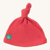 Little Green Radicals pink berry waffle tie hat available at Babipur. A GOTS organic cotton hat in pink with a knot on the top. Features a small brand patch on the brim