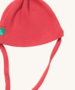 A close up of the Little Green Radicals pink berry waffle tie hat showing the tie strap for a secure fit and waffle knit detail on pink organic cotton fabric