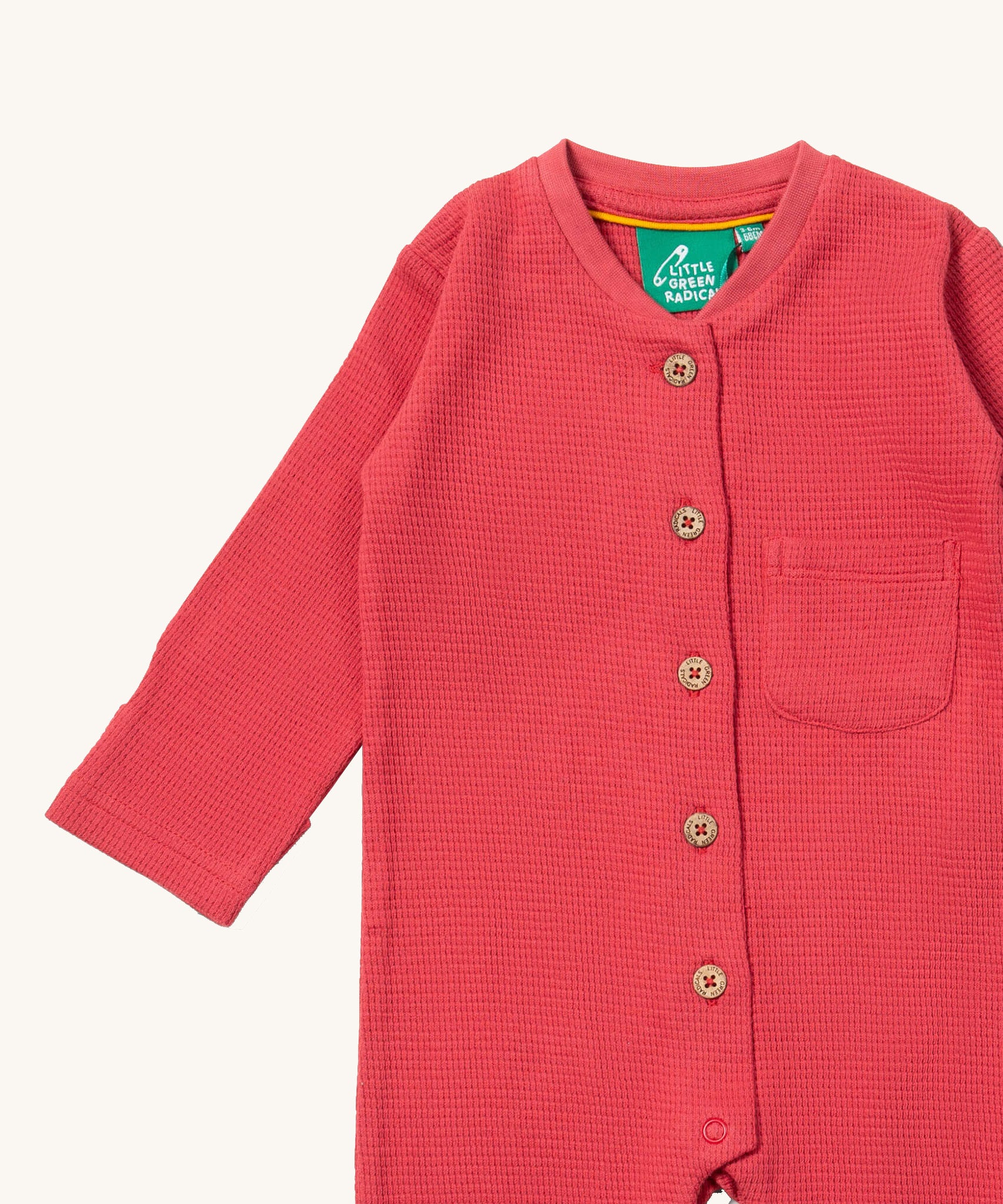 A close up of the Little Green Radicals pink waffle playsuit showing the button fastener detail and waffle detail. 