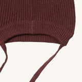 A close up of the Little Green Radicals chocolate knitted beanie hat showing the brown tie detail on and elasticated brim on brown organic cotton fabric.