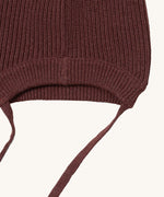 A close up of the Little Green Radicals chocolate knitted beanie hat showing the brown tie detail on and elasticated brim on brown organic cotton fabric.