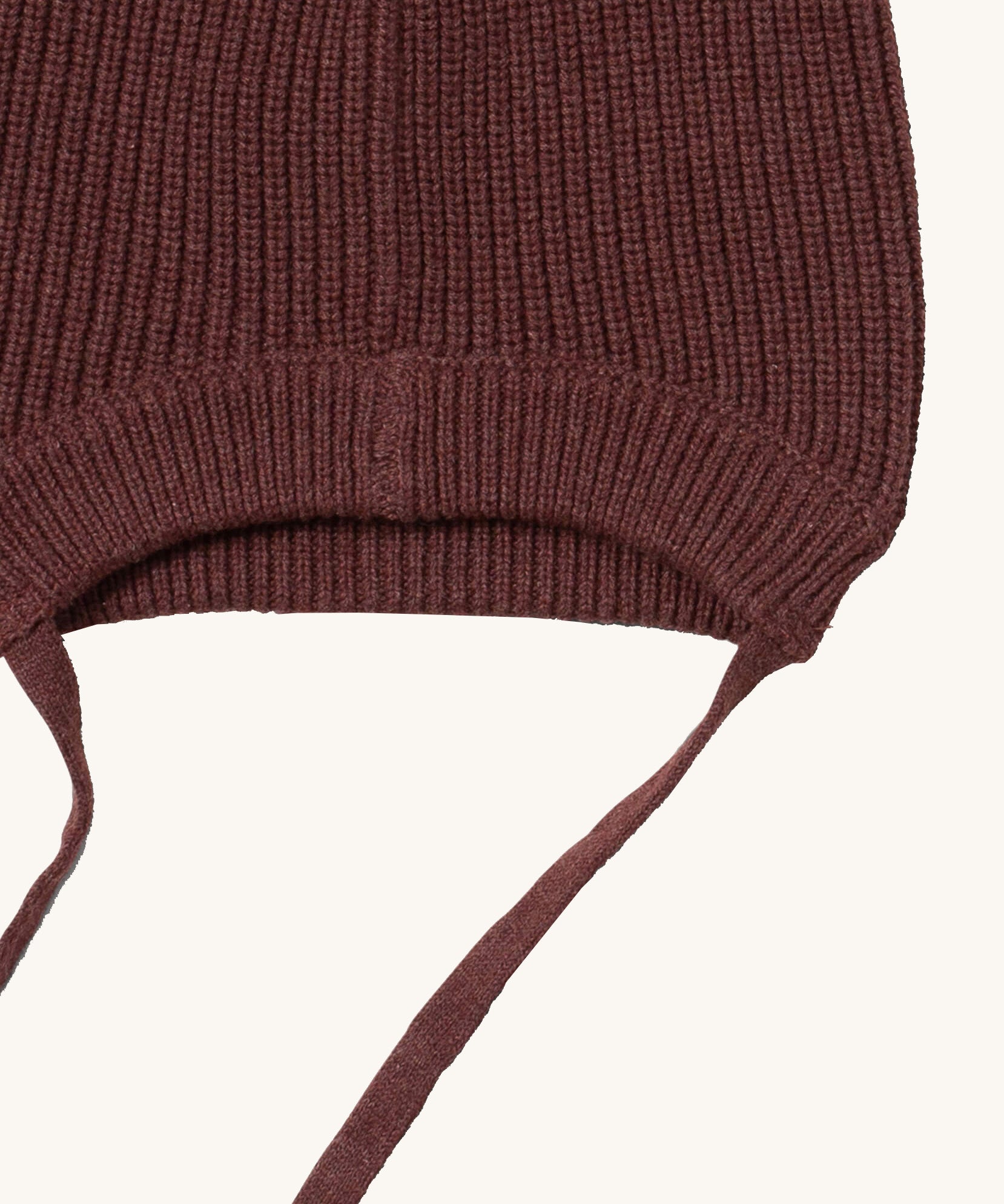 A close up of the Little Green Radicals chocolate knitted beanie hat showing the brown tie detail on and elasticated brim on brown organic cotton fabric.