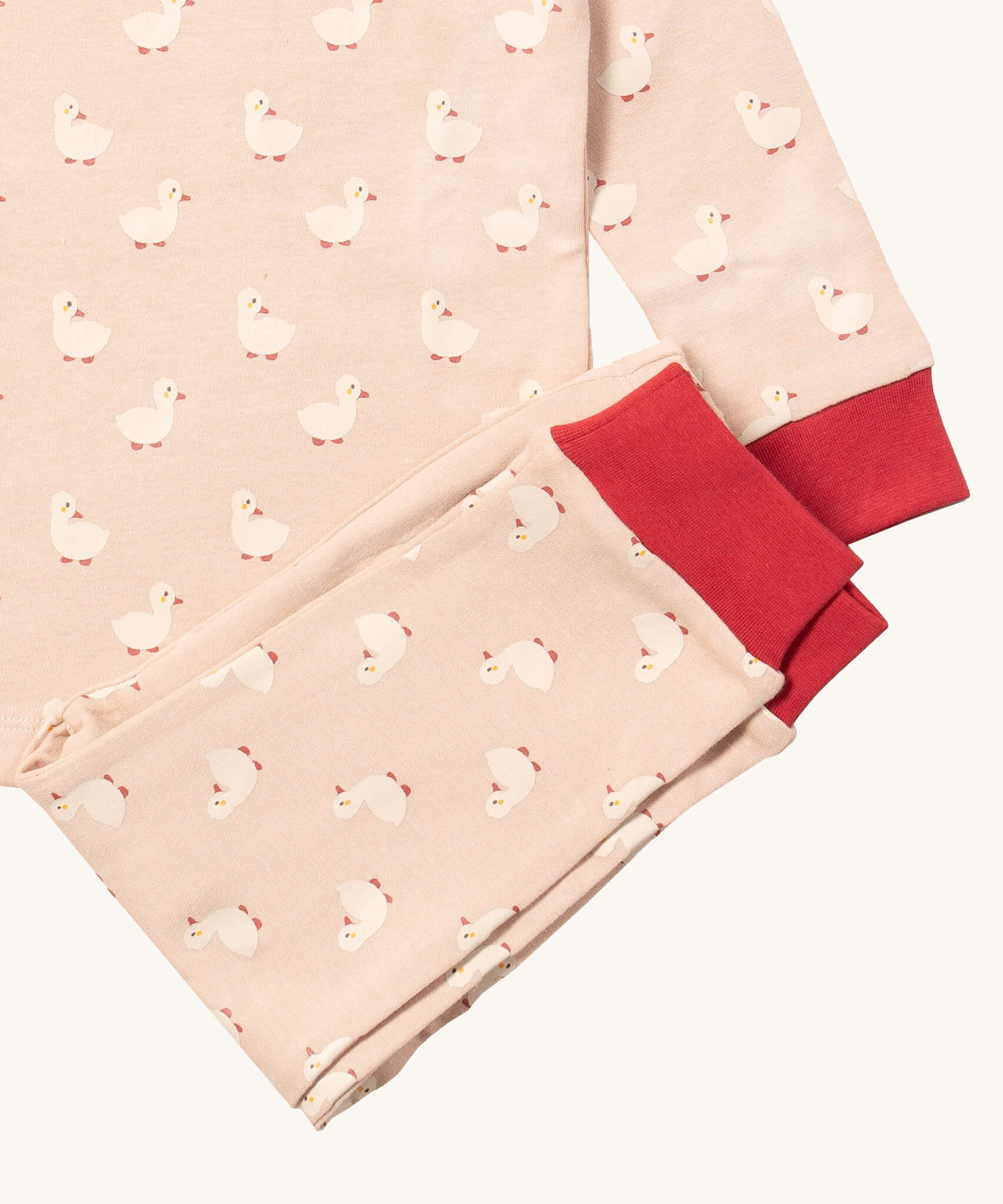 A close up of the Little Green Radicals puddle ducks pyjama set showing the red cuff trim detail and the white duck print detail on light pink organic cotton fabric.