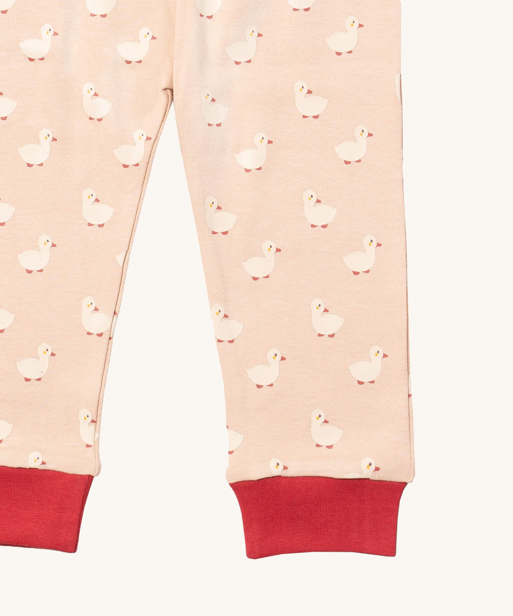 A close up of the Little Green Radicals puddle duck pyjama bottom. Showing the red cuff detail with a close up of the white duck print on light pink organic cotton fabric.