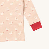 A close up of the Little Green Radicals puddle ducks top showing the red elasticated cuff detail with a close up of the white duck print on light pink organic cotton fabric.