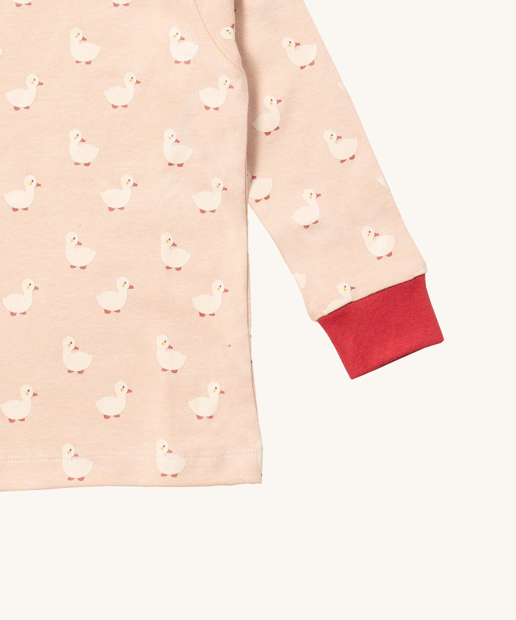 A close up of the Little Green Radicals puddle ducks top showing the red elasticated cuff detail with a close up of the white duck print on light pink organic cotton fabric.