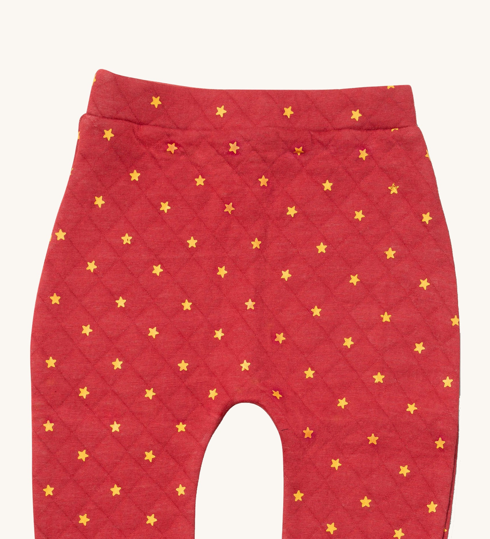A close up of the Little Green Radicals red star quilted joggers. Showing the quilted stitch and yellow stars detail on red organic cotton fabric.