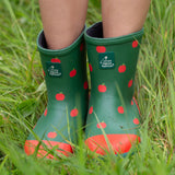 A child wearing the Little Green Radicals kid wellington boots showing the length of the boots and the red apples print on the natural rubber material. Features a brand patch on the front of the wellington.