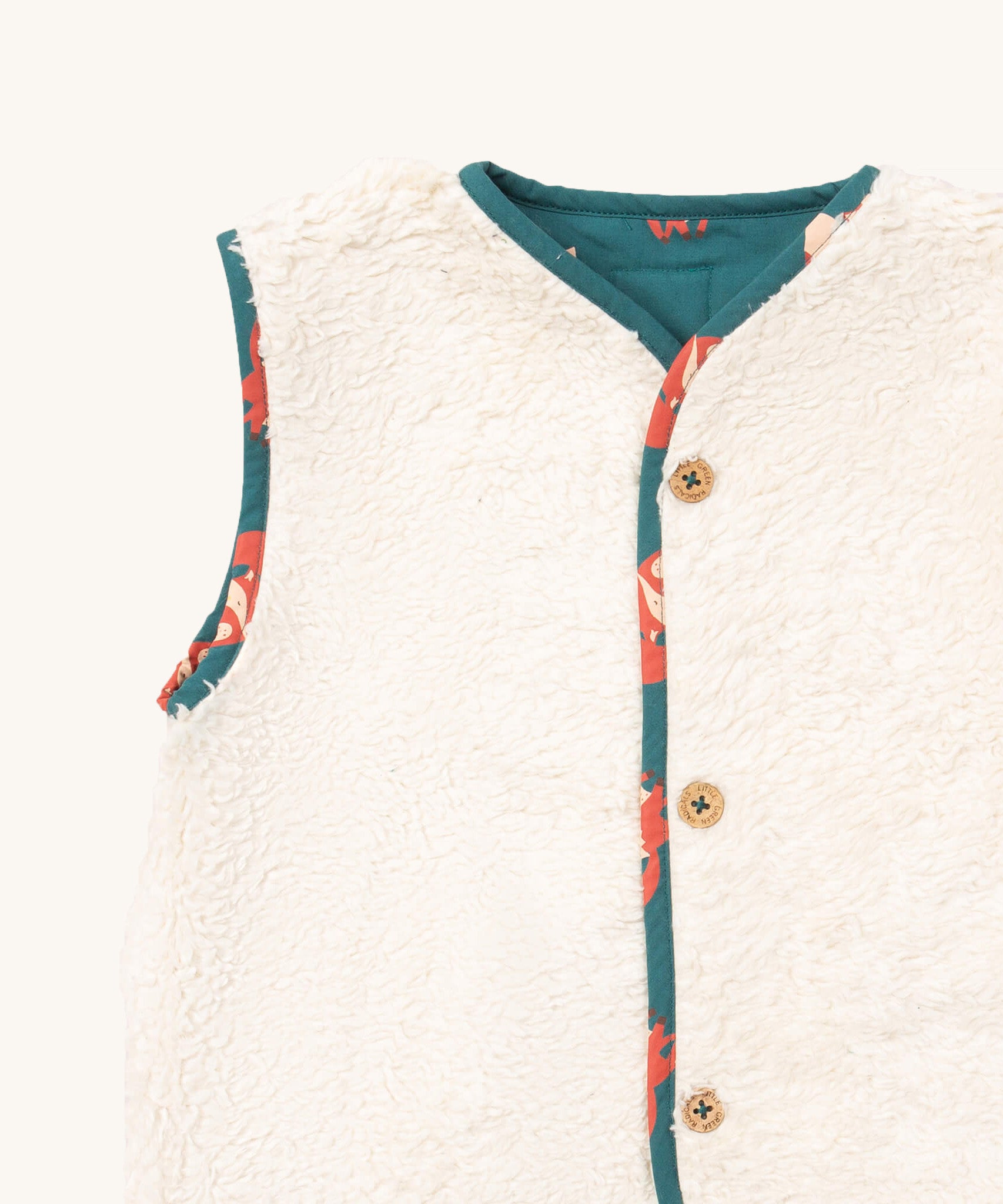 A close up of the Little Green Radicals reversible gilet in red foxes and sherpa lined. Showing the white sherpa fleece and button detail.
