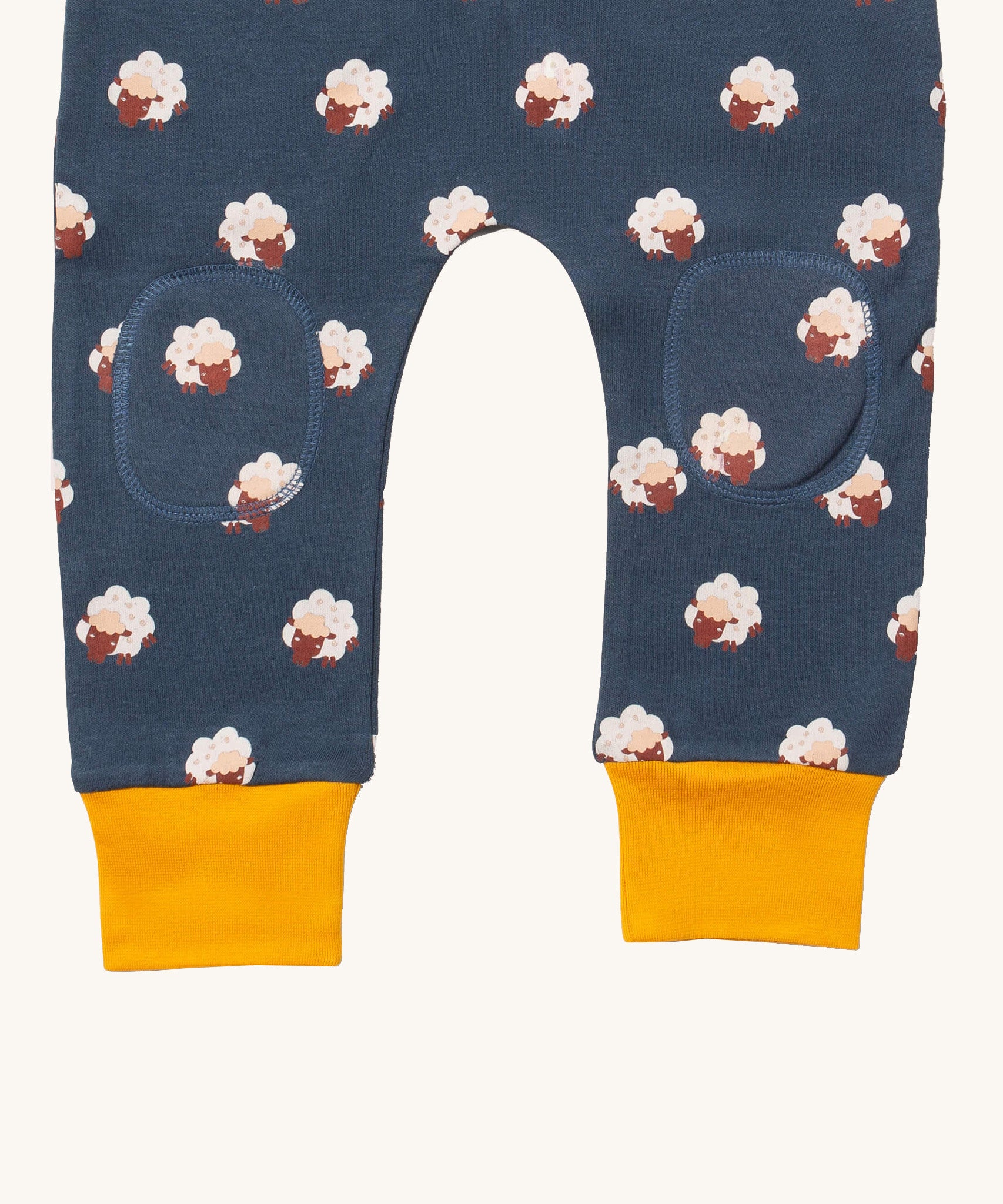 A close up of the Little Green Radicals comfy joggers in sleeping sheep showing kneepatch detail and yellow cuff trim on navy organic cotton fabric
