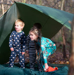 Children standing outside a tent in the forest. They are all wearing Little Green Radicals organic cotton pyjamas. One is wearing a pair with the Winter Rabbit on them, one in wearing navy and white striped design and the third is wearing the sleeping sheep print. Little green Radicals have a wide range of organic cotton, Fairtrade children's clothing an outerwear available here at Babipur.