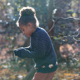 A child wearing the Little Green Radicals navy sheep snuggle knitted jumper outside showing the length and fit of the GOTS organic cotton jumper. 