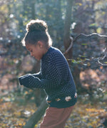 A child wearing the Little Green Radicals navy sheep snuggle knitted jumper outside showing the length and fit of the GOTS organic cotton jumper. 