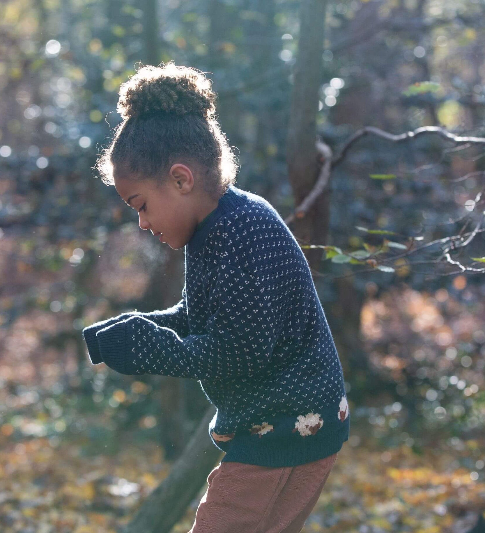 A child wearing the Little Green Radicals navy sheep snuggle knitted jumper outside showing the length and fit of the GOTS organic cotton jumper. 