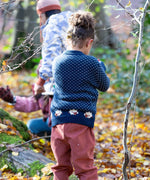 A child wearing the Little Green Radicals navy sheep snuggle knitted jumper outside showing the white speckles and cute sheep continuing around the jumper