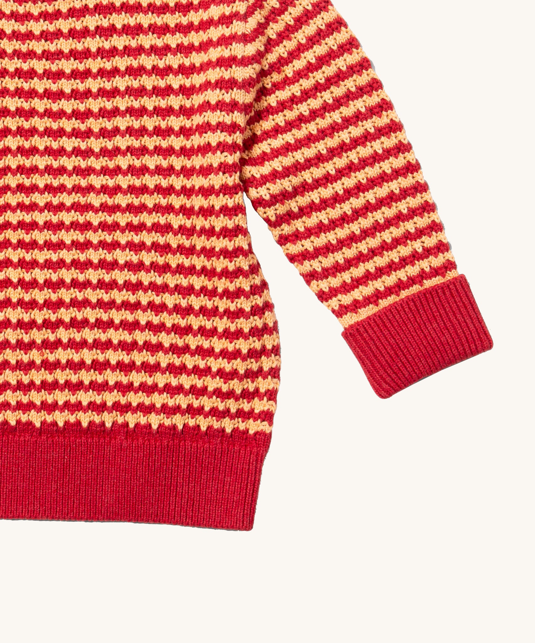 A close up of the Little Green Radicals snuggly knitted jumper in juniper stripe available at Babipur. Showing the yellow and pale red stripe knit detail and the matching pale red turned up cuff for size adjusting