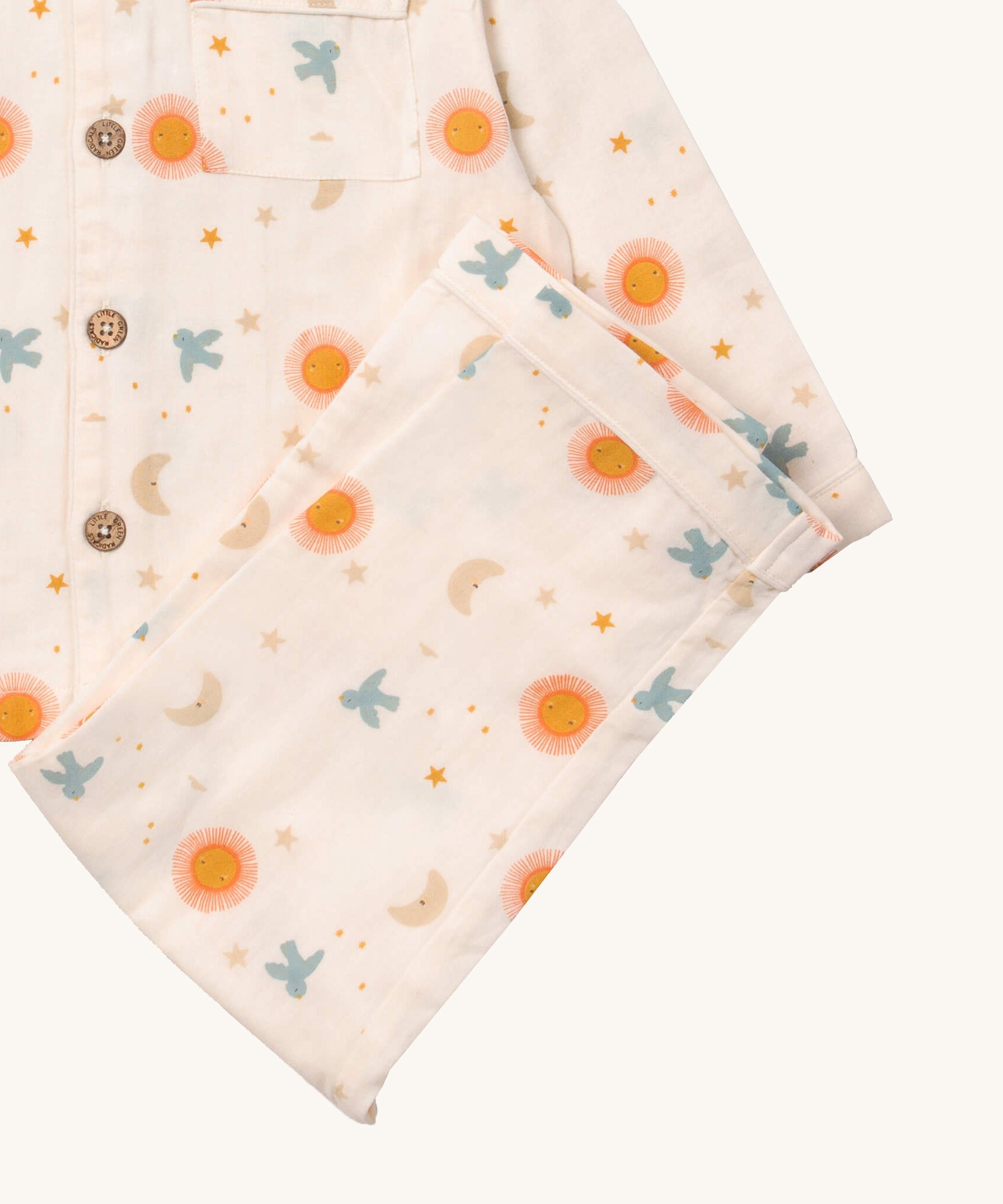 A close up of the Little Green Radicals classic moon and sun pyjama set showing the light pink organic cotton bottoms laid on top of the matching pyjama top.