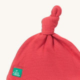A close up of the Little Green Radicals pink berry waffle tie hat showing the knot detail and waffle knit detail on pink organic cotton fabric