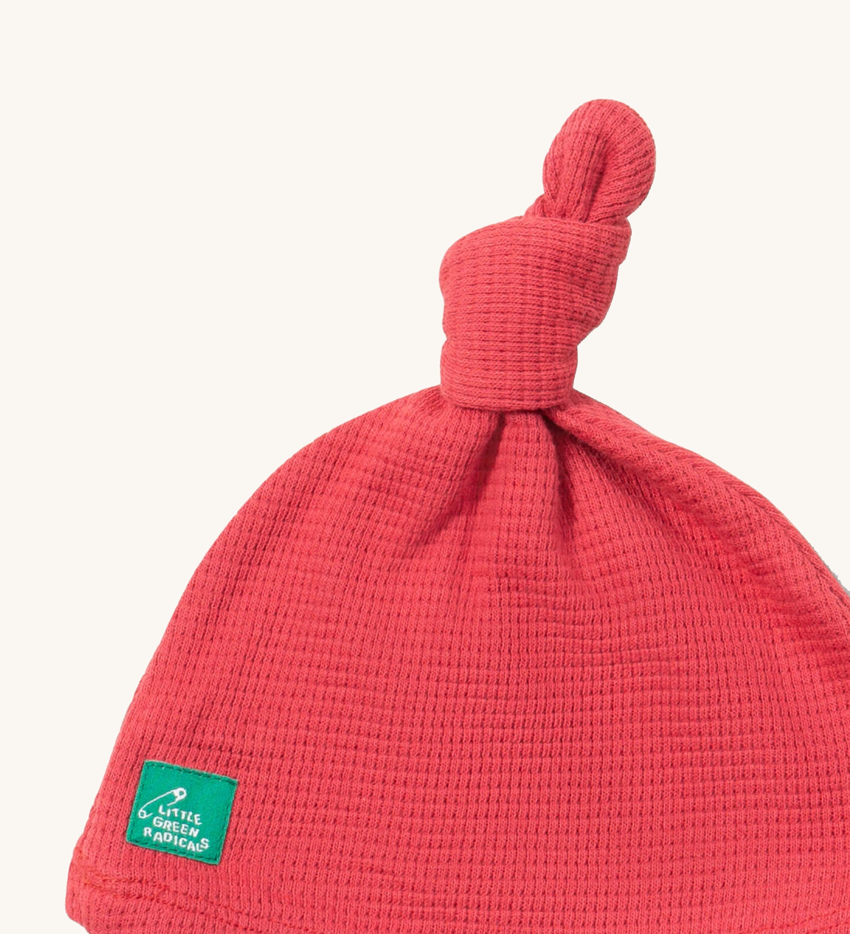 A close up of the Little Green Radicals pink berry waffle tie hat showing the knot detail and waffle knit detail on pink organic cotton fabric