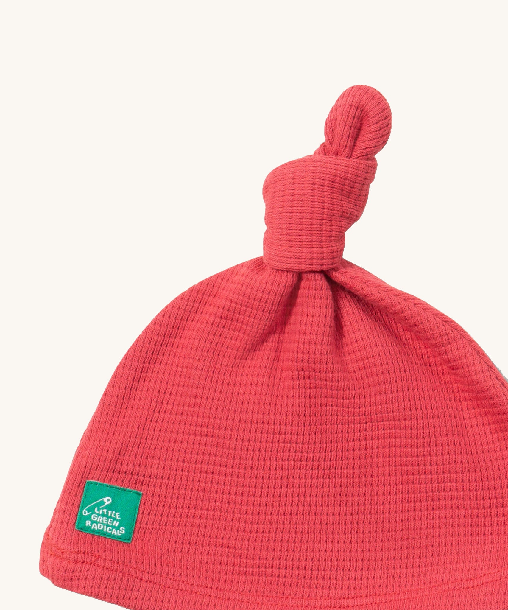 A close up of the Little Green Radicals pink berry waffle tie hat showing the knot detail and waffle knit detail on pink organic cotton fabric