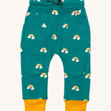 Little Green Radicals comfy joggers in turquoise rainbow available at Babipur.. A soft GOTS organic cotton turquoise jogger pants with yellow trim and cute rainbow prints. Features 2 side pockets a matching navy waist drawstring and knee patches.