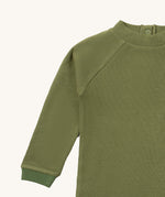 A close up of the Little Green Radicals green chive waffle long sleeve cosy top showing the waffle and popper fastener detail on green organic cotton fabric