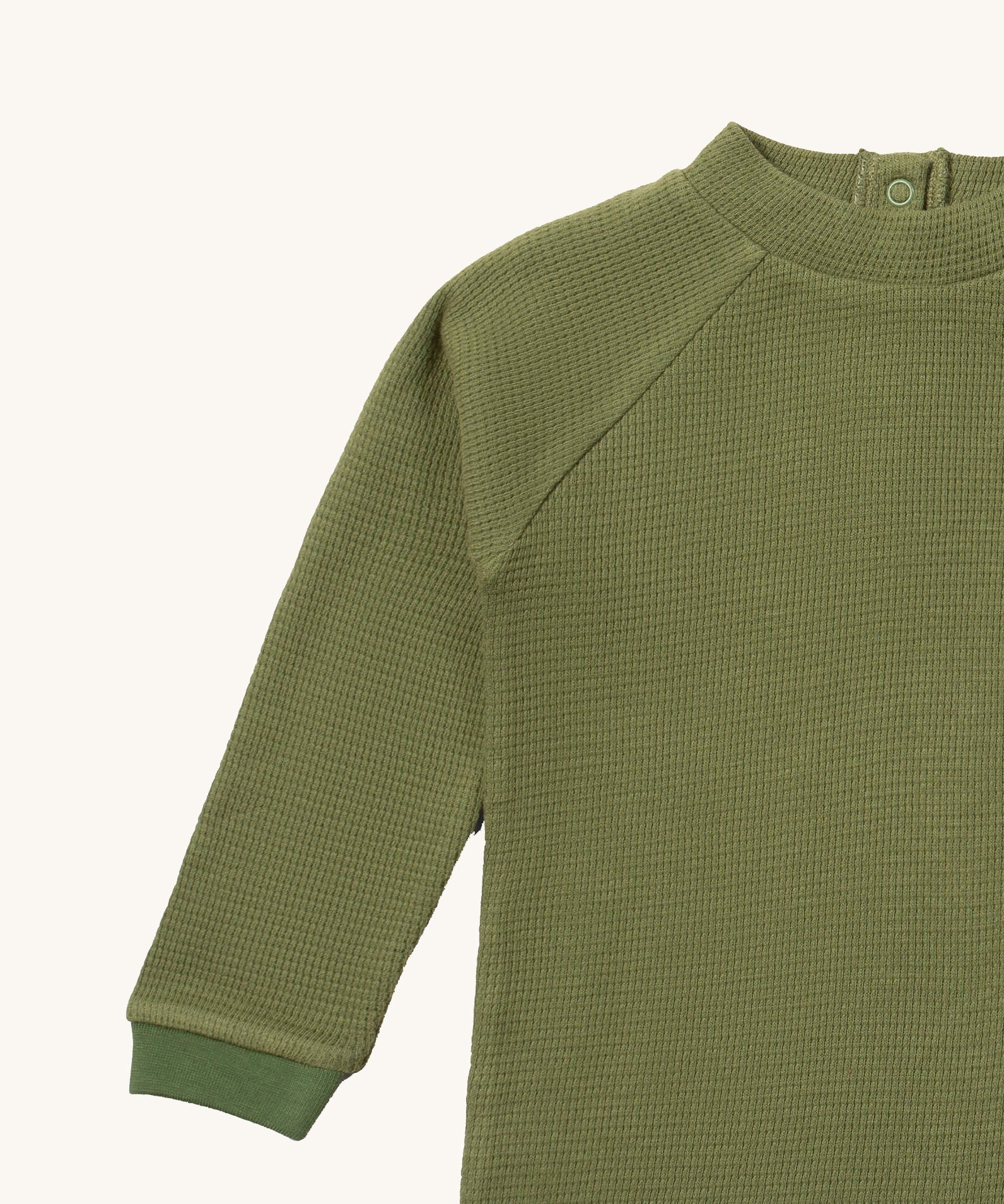 A close up of the Little Green Radicals green chive waffle long sleeve cosy top showing the waffle and popper fastener detail on green organic cotton fabric
